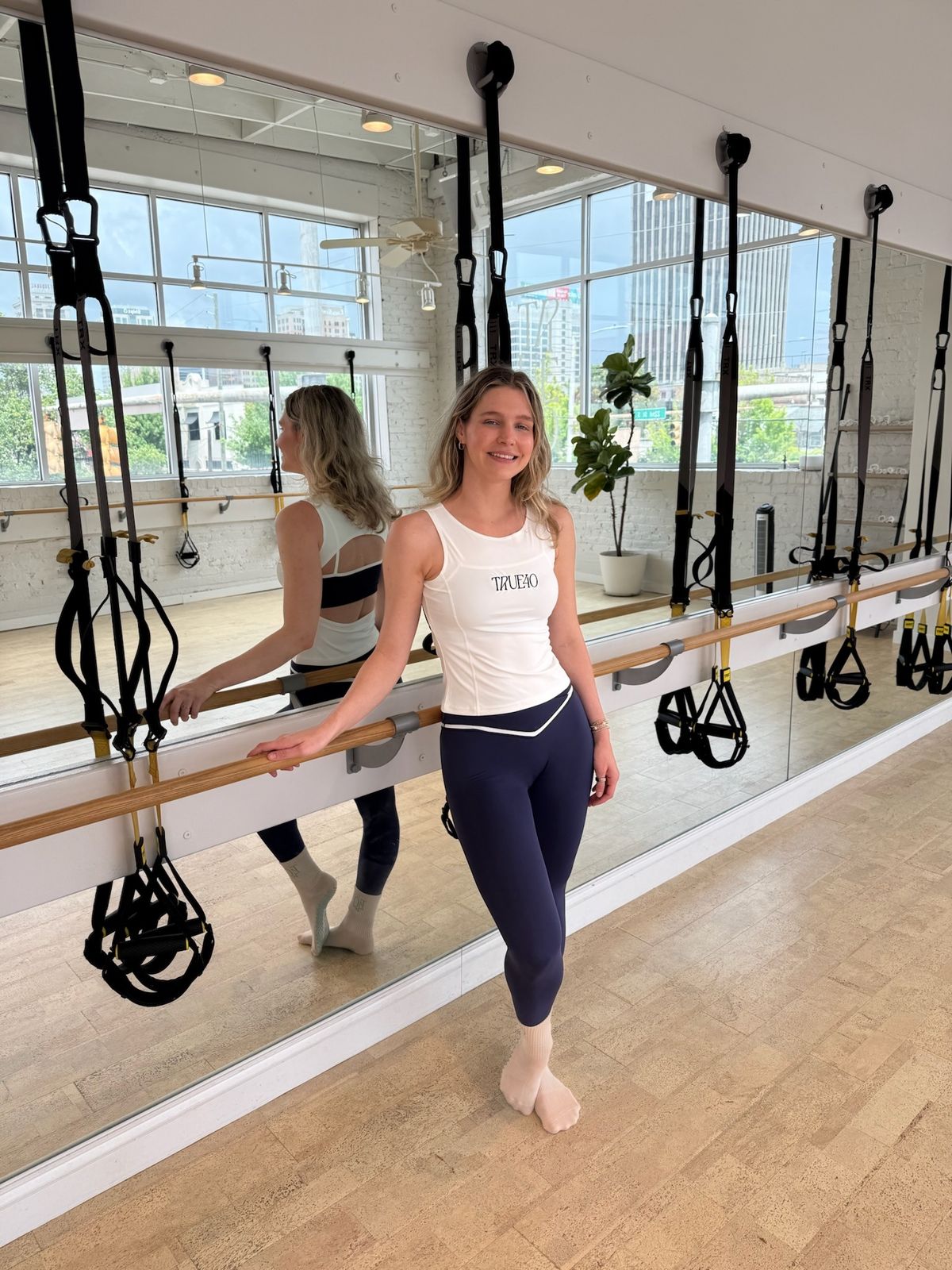Model wearing the fitted white True40 logo tank in the True40 Fitness studio.