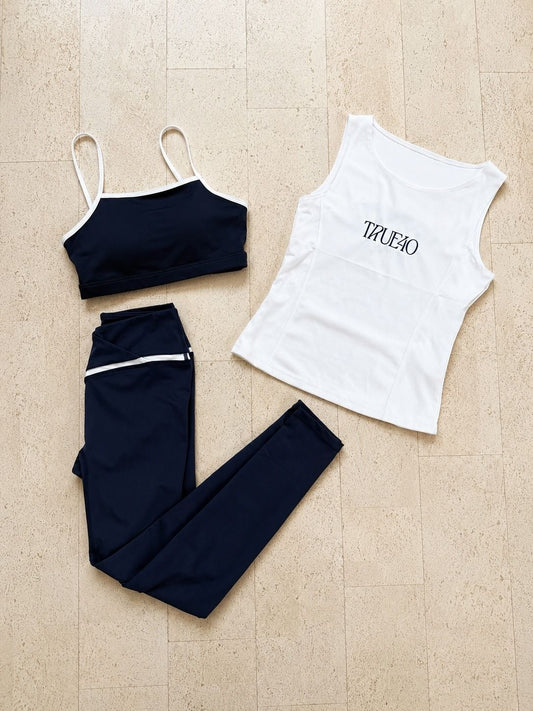Flat lay of a True40 navy sports bra, white logo tank and navy leggings with white trim.